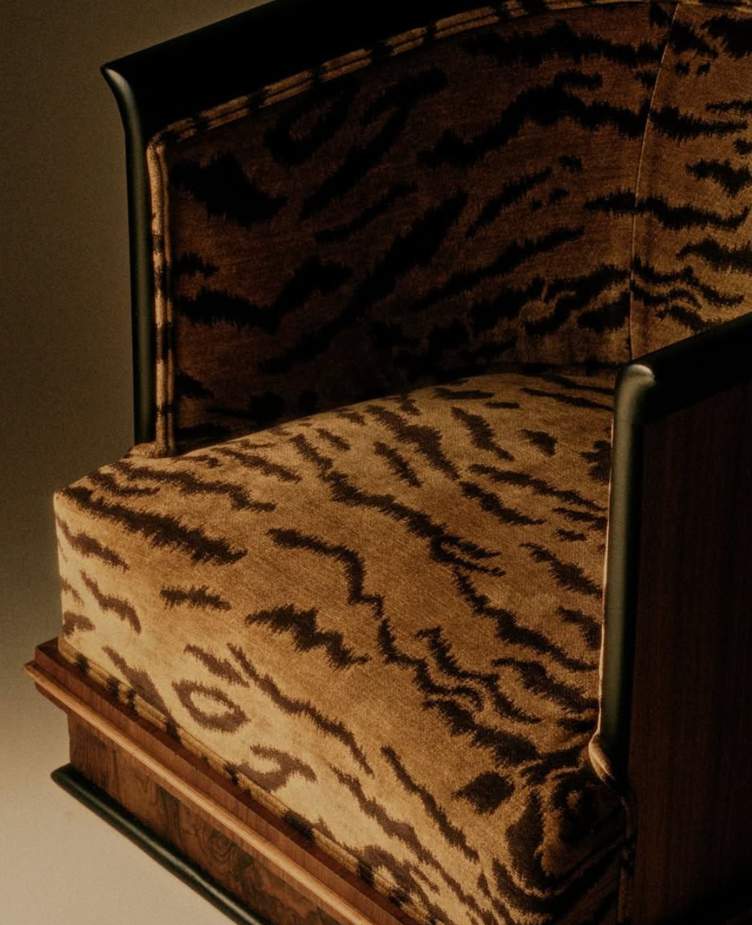 A close-up of a luxury armchair upholstered in a brown and beige tiger-stripe patterned fabric, featuring dark wood arms and base.
